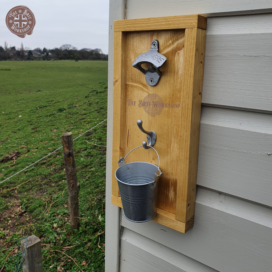 Rustic wall mounted bottle opener UK countryside background, fixed to wood cladded wall outside with cap catcher bucket. antique pine wood with hammered silver metal style ironmongery